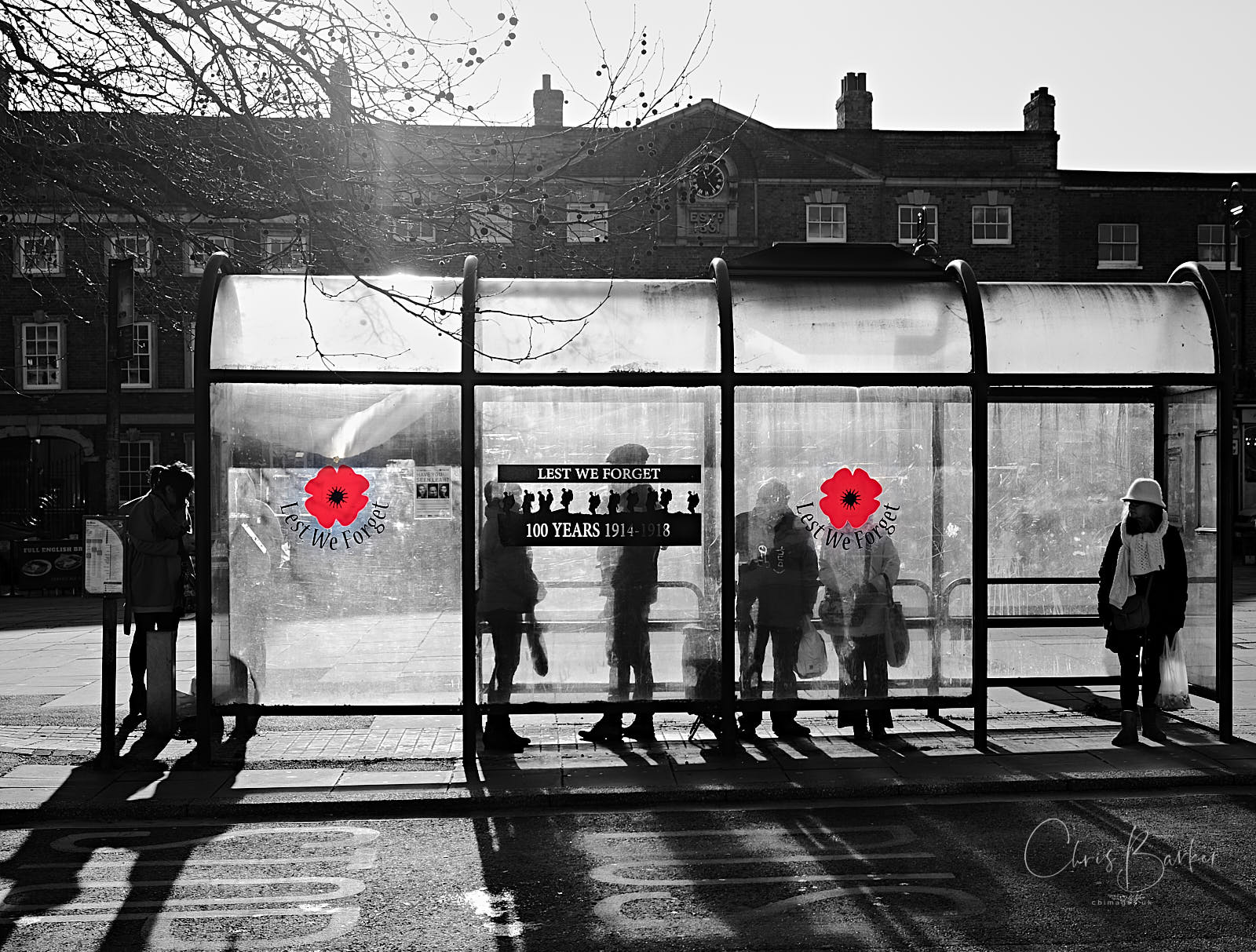 Silhouettes of people in a perspex bus shelter with red poppy designs on the perspex and Lest We Forget between