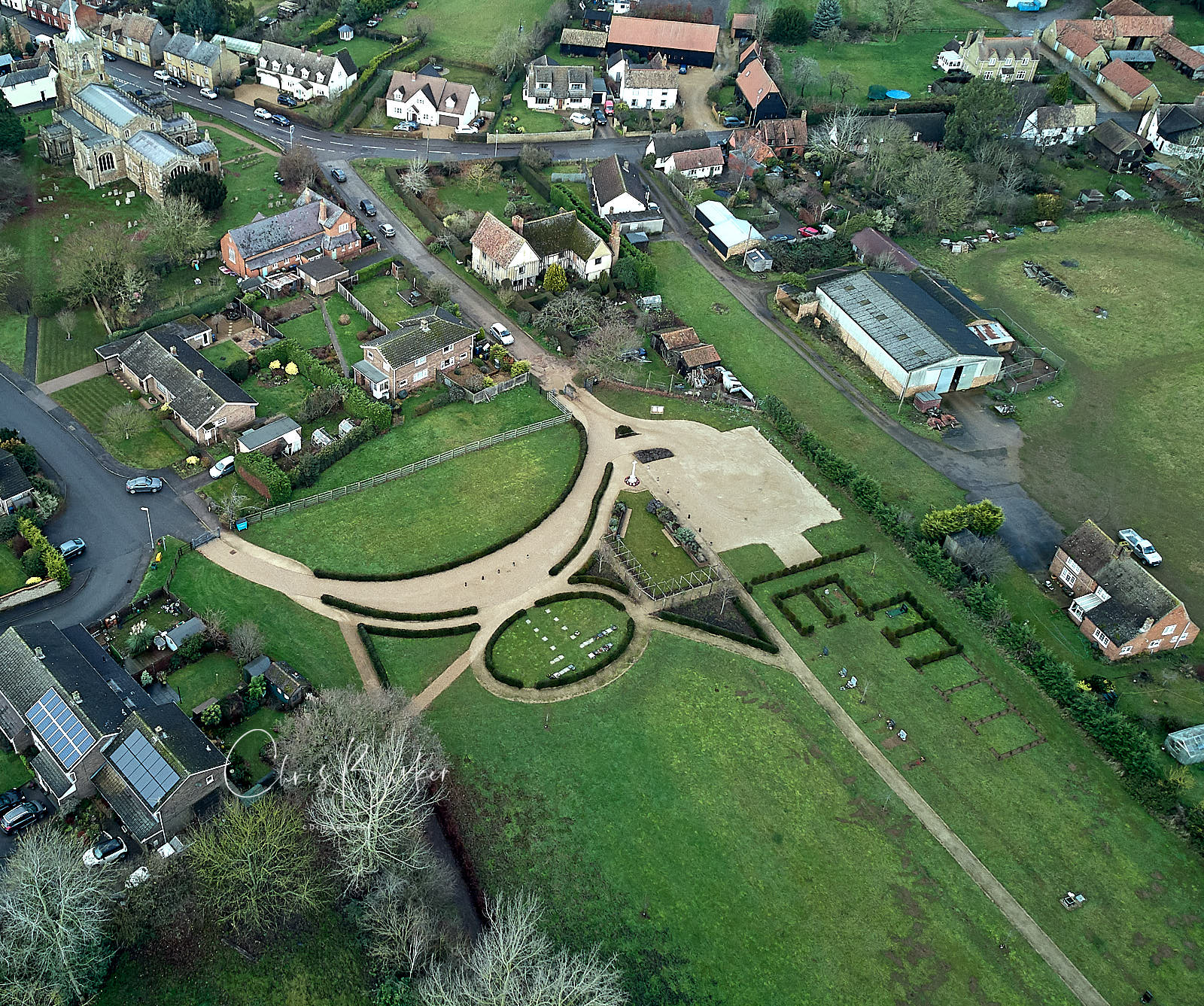 God's eye view of a new green graveyard on the edge of a village, some houses visible, the old Anglican church in the top left corner